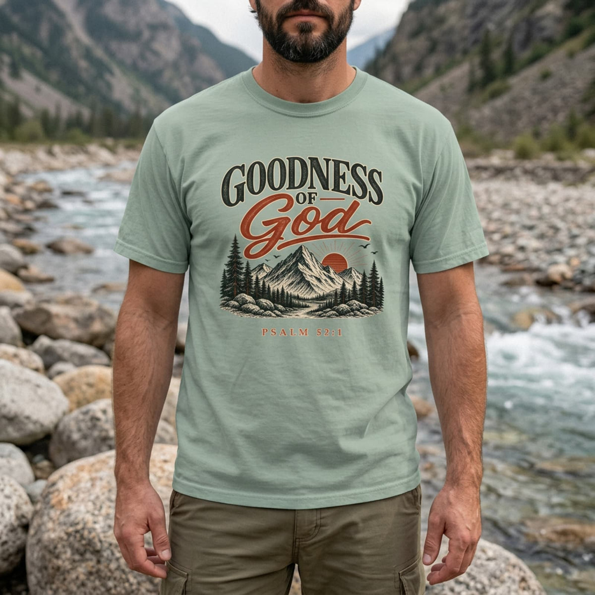 Close-up of a man by a mountain river wearing the Bay Goodness of God Psalm 52:1 t-shirt