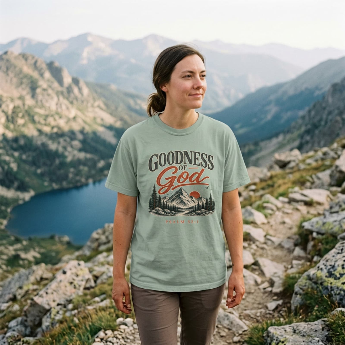 Woman on a mountain ridge above an alpine lake wearing the Bay Goodness of God Christian hiking t-shirt
