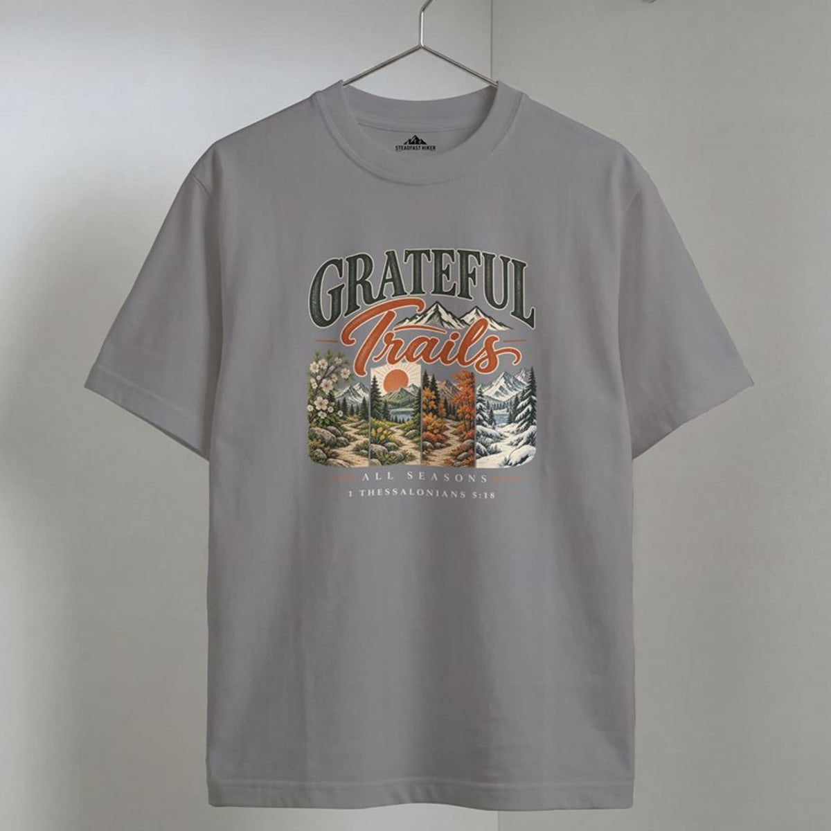 Grey Grateful Trails Christian hiking t-shirt on a wooden hanger, 1 Thessalonians 5:18