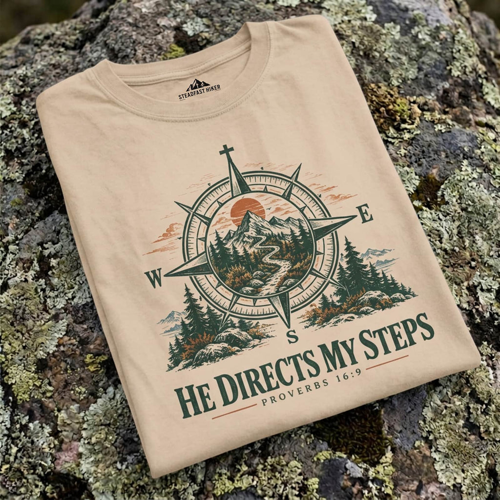 Ivory He Directs My Steps t-shirt folded on a lichen-covered rock, close-up of the compass print