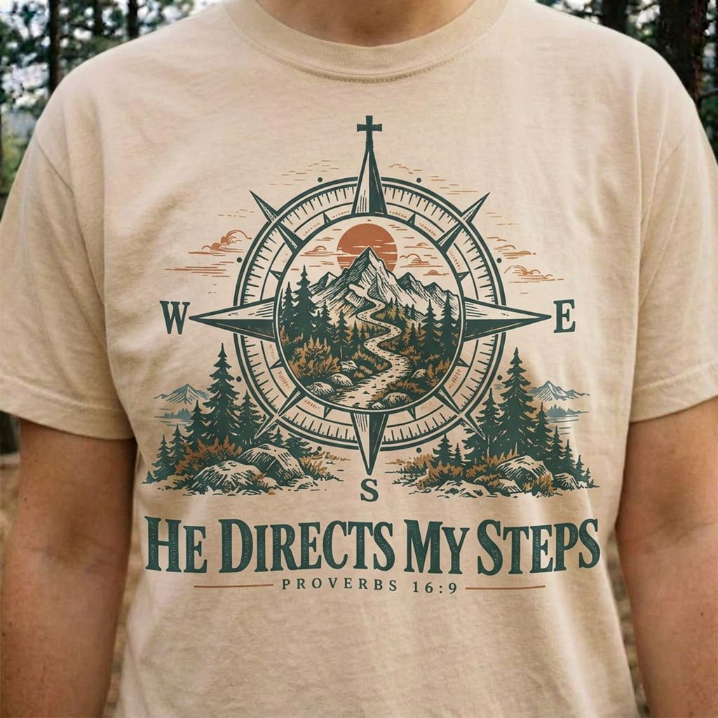 Close-up of the compass print on an Ivory He Directs My Steps t-shirt worn on a forest trail
