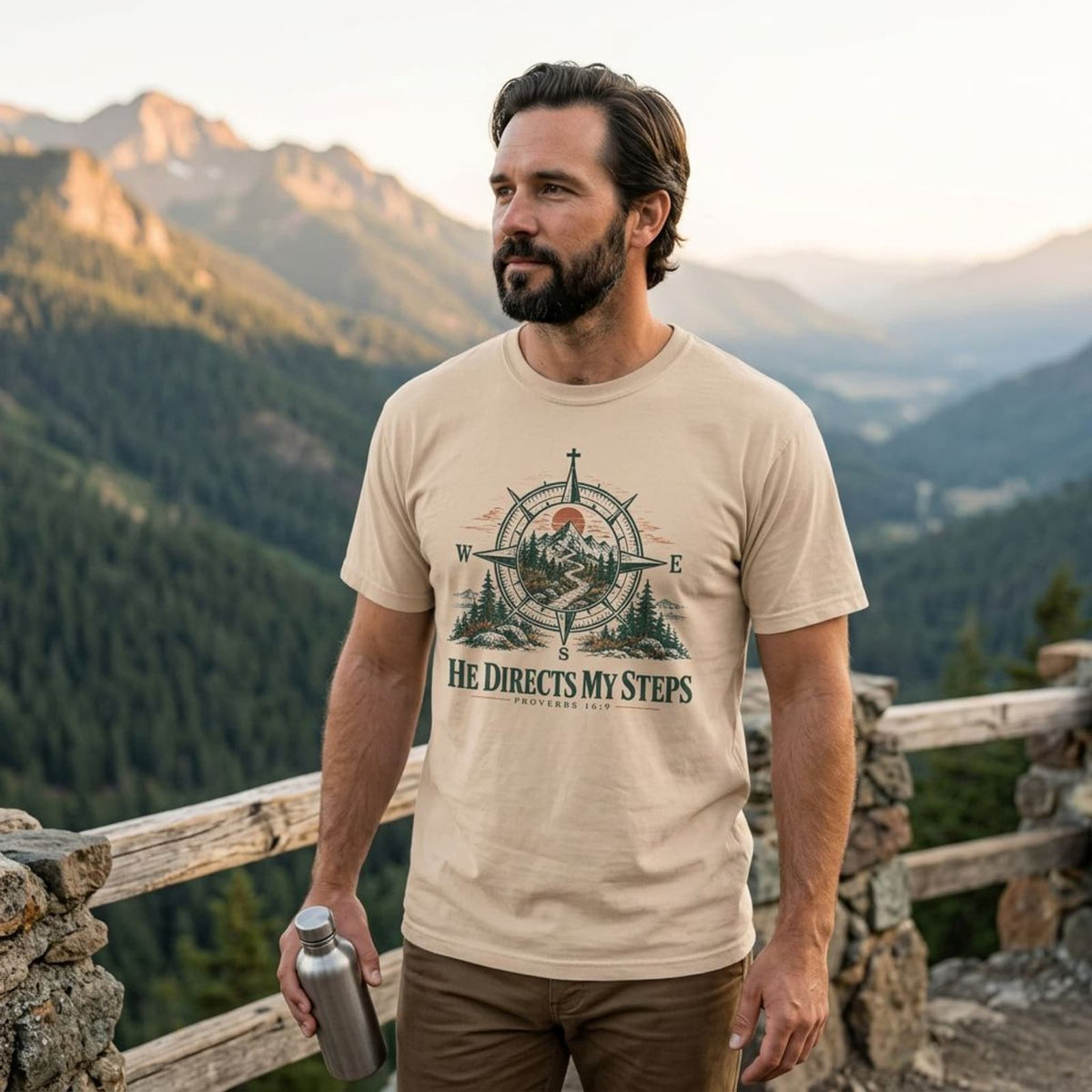 Bearded man at a mountain overlook wearing the Ivory He Directs My Steps t-shirt at sunset