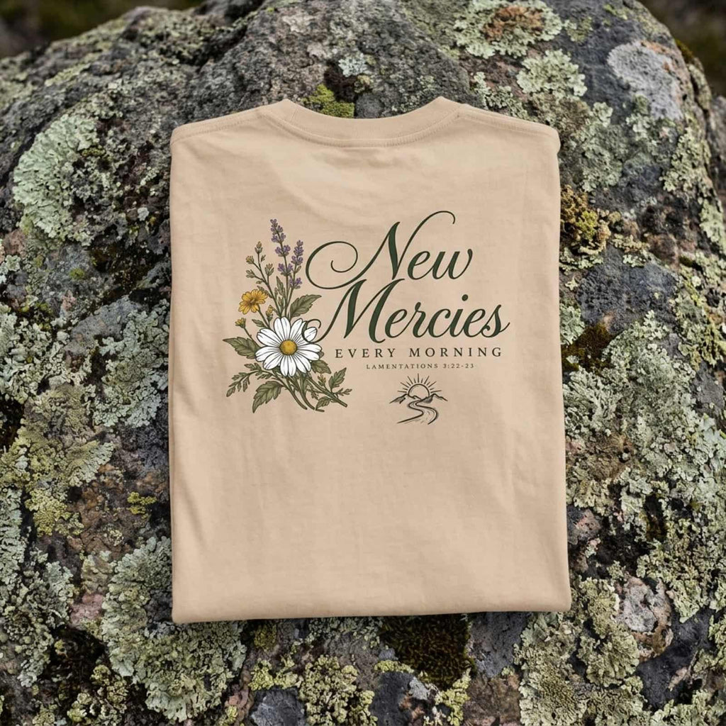 Folded Ivory New Mercies t-shirt showing the daisy and wildflower back print on a lichen-covered rock