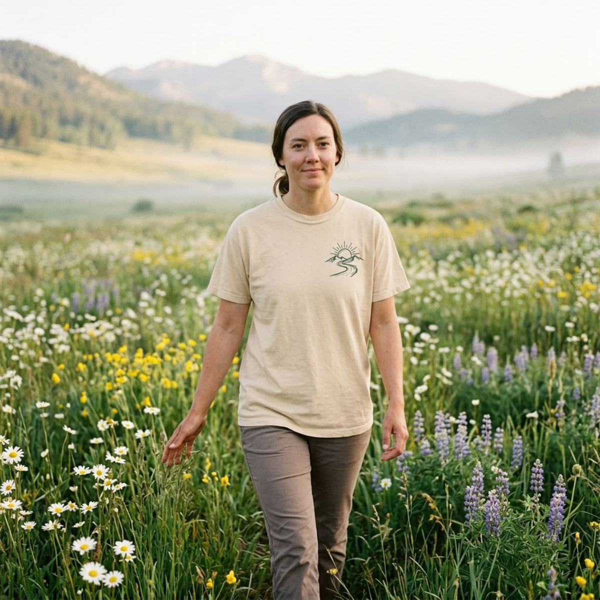 Woman walking through a wildflower meadow wearing the Ivory New Mercies Christian hiking t-shirt