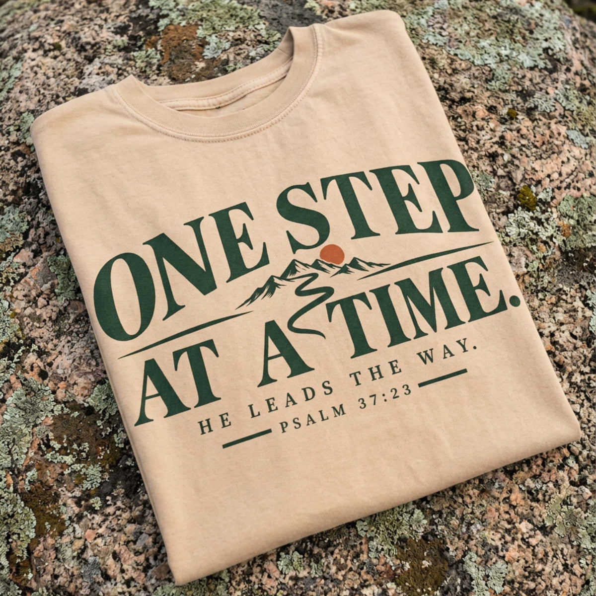 Close-up of the One Step at a Time design printed on an Ivory Christian hiking t-shirt resting on a rock, Psalm 37:23