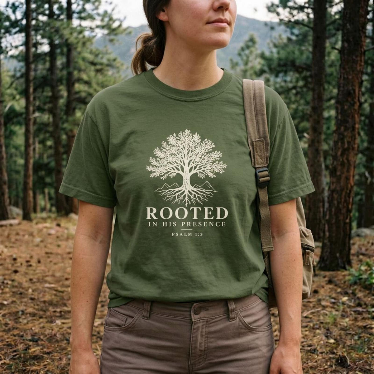 Woman in a pine forest wearing the Sage green Rooted In His Presence Christian hiking t-shirt