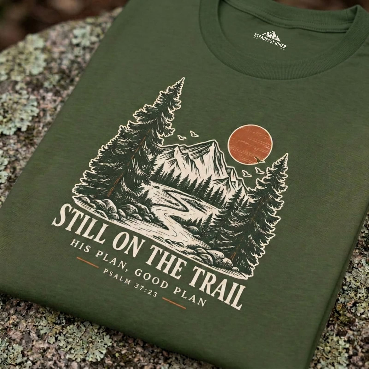Still on the Trail Christian hiking T-shirt in ivory with a vintage mountain and faith design, displayed on a natural rock surface.