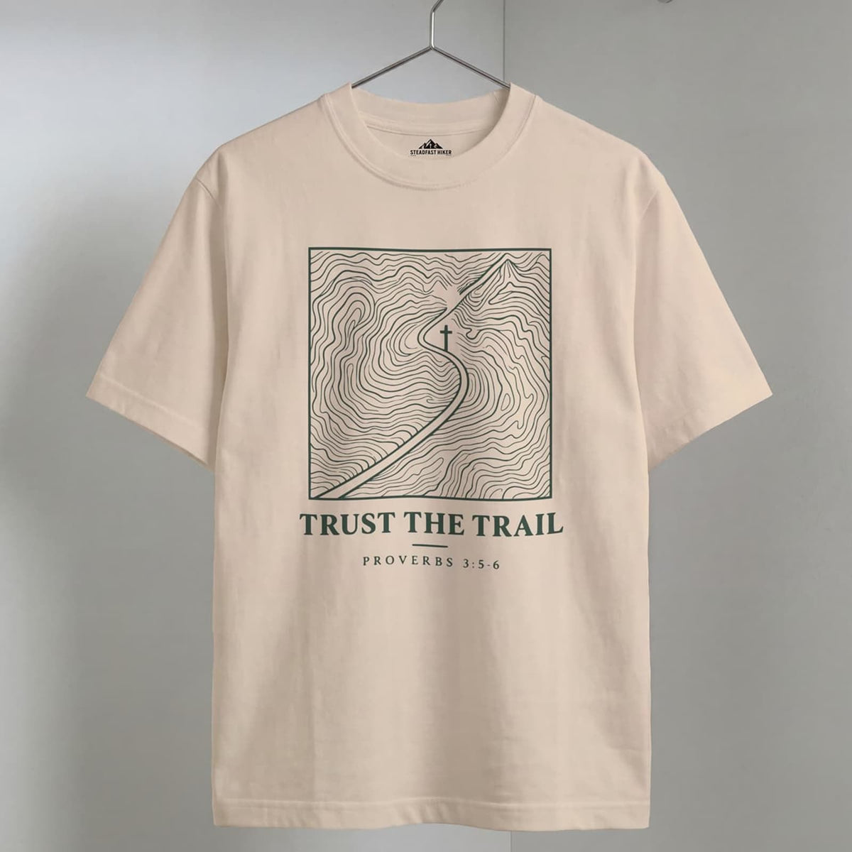 Ivory Trust the Trail Christian hiking t-shirt on a wooden hanger