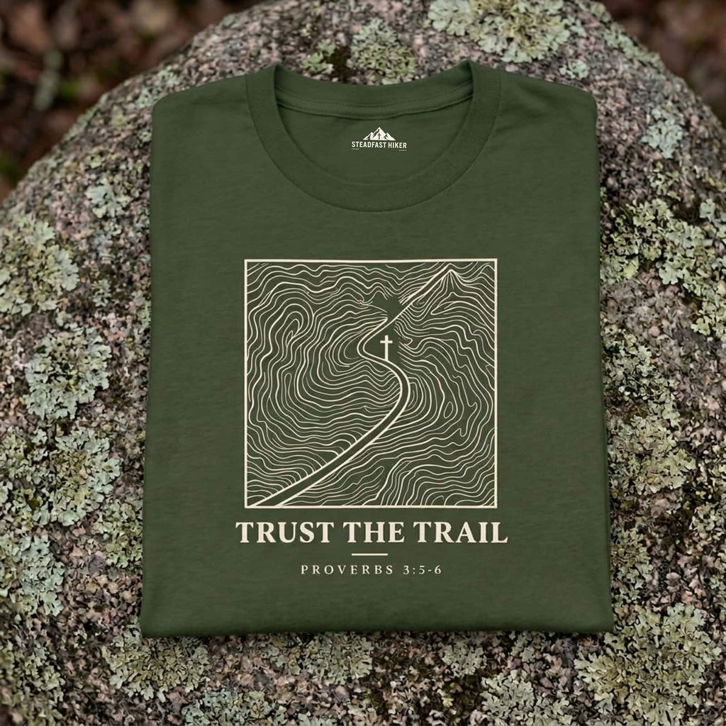 Close-up of the Trust the Trail topographic trail map design printed on a Sage Christian hiking t-shirt resting on a rock, Proverbs 3:5-6